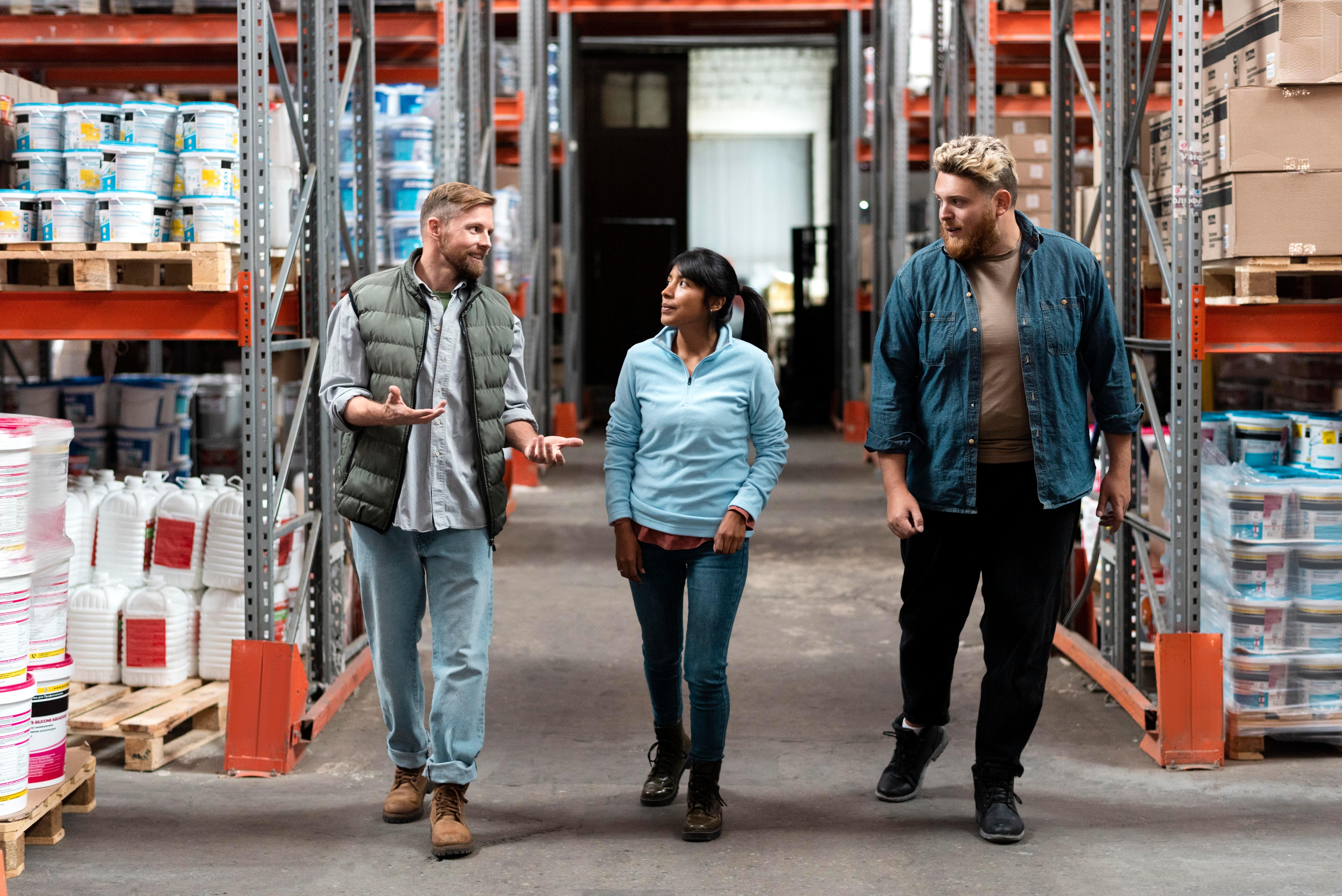 Two men and a woman conversing while walking in a warehouse
